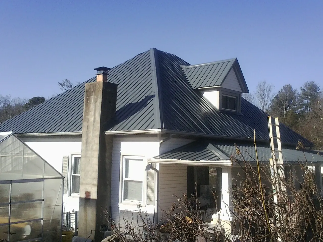 Dark blue standing seam metal roof on a white farmhouse with dormer — Slate & Tile Roof Repair by Roofing Brothers in Blessing
