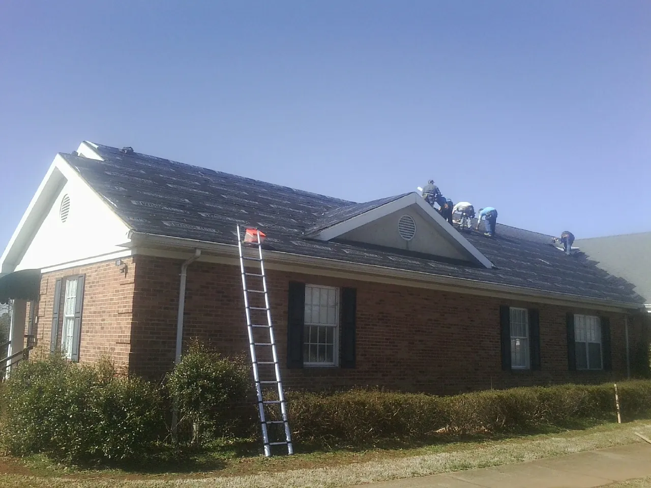 Crew tearing shingles off a brick ranch roof with a ladder set — Metal Roof Repair work by our crew in Blessing