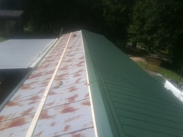Old rusted panels beside newly installed green metal roofing — Wind Damage Roof Repair by Roofing Brothers in Blessing