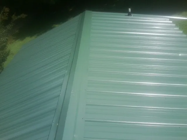 New green metal panels meeting at the ridge of a roof — Flat Roof Repair work by our crew in Blessing