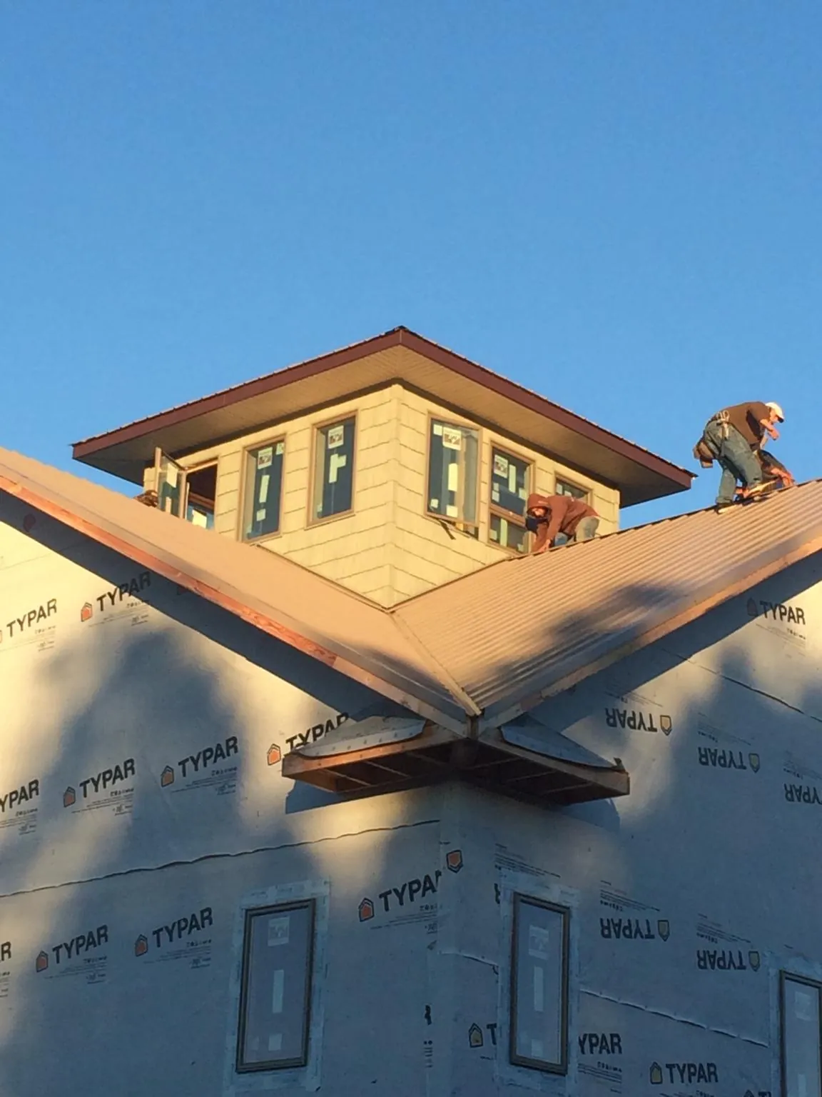 Roofers working around a rooftop cupola on a new metal roof at sunset — Roof Waterproofing in Blessing by Roofing Brothers